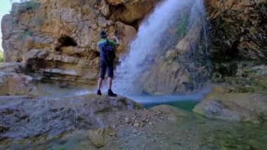 Adam elinde bir cep telefonu tutuyor ve güzel bir şelalenin fotoğrafını çekiyor.. 