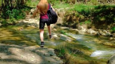 Woman is crossing a river. Girl is hiking in nature.