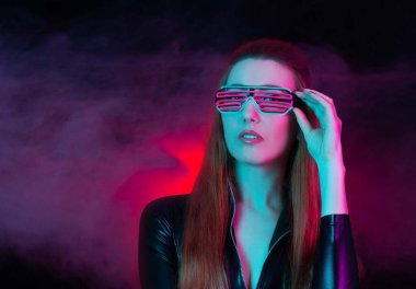 Neon ışıklı gözlüklü gelecekten gelen bir kadın. Uzun saçlı bir mankenin portresi. Deri elbise kostümü. Geleceğin güzelliği. Renkli arkaplan. 
