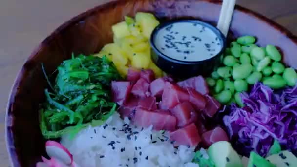 ボウルを閉じてください 木製のテーブルの上にボウルサラダをポーク 新鮮な野菜 生の魚 海苔のわかめ アボカド マンゴー 健康食品 アジアンランチ — ストック動画