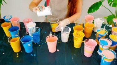 Bir sanatçı akrilik renkleri karıştırıyor. Farklı renkte boyanmış bir sürü plastik bardak. Sıvı resim hazırlama.