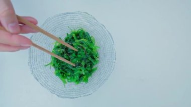 Close up of an algae with chopsticks. Soaked green wakame seaweed in a glass bowl. Japanese food. Healthy seafood. Slow motion video. Isolated on white. Top view. 