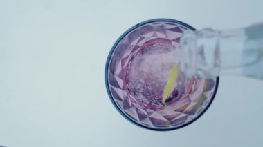 Şişeden çıkan gazla suyu buzlu ve limonlu bardağa doldurun. Üst Manzara. Su akışı ağır çekimde düşüyor. Beyaz arkaplanda bardağa dökülen temiz bir sıvının tazeliği. 