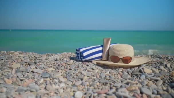 Hat Sunglasses Sun Cream Towel Laying Stony Beach Blue Turquoise — ストック動画