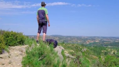 Man is standing with a laying backpack. Hiking in nature. Beautiful landscape from a cliff. Concept of freedom and happiness. Horizontal video in a slow motion.