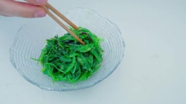 Close up of an algae with chopsticks. Soaked green wakame seaweed in a glass bowl. Japanese food. Healthy seafood. Slow motion video. Isolated on white. Top view. 