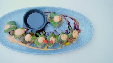 Chopsticks Dipping Sushi Roll into Soy Sauce. Asian traditional food on a ceramic plate. Tasty vegetarian healthy dish. Slow motion horizontal video.