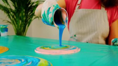 Sıvı sanat tekniği. Kadın sanatçı, akrilik renkleri karıştırarak soyut akışkan sanat eserleri üzerinde çalışıyor. İşlem halindeki ressam bir sanat stüdyosunda sanat eseri yaratıyor. Yavaş çekim videosu. 