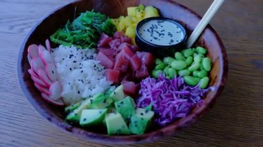 Bir kâseyi kapat. Tahta bir masada kase salatası. Dilimlenmiş taze sebze, çiğ balık, edamame fasulyesi, yosun wakame, avokado, mango, pilav, diyet yemeği. Sağlıklı yiyecekler. Asya yemeği.