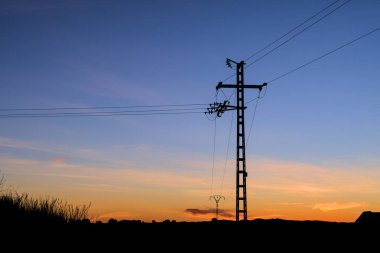 Gece karanlığında elektrik direğinin silueti. Elektrik kablolarının üzerinde gün batımı. Temiz enerji. Yüksek voltajlı elektrik kulesi. 