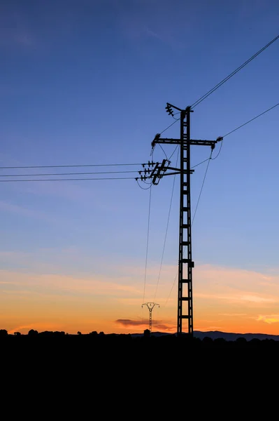 Silhouette of an electric pole on dusk background. Sunset over the electric power lines. Clean energy. High voltage electric power tower.