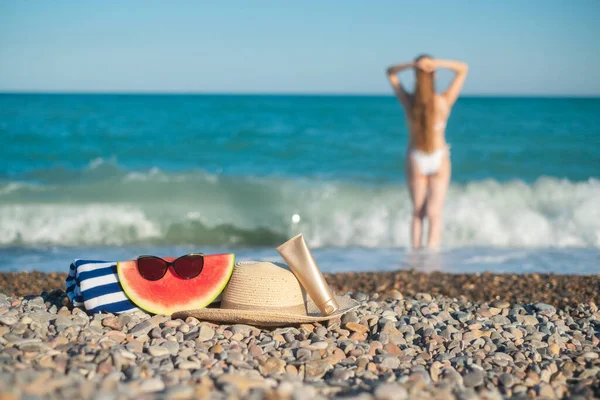 Hat, a towel and sunglasses. Tall woman with a long hair from a back is on a beach. Mediterranean sea with waves on the background. Blue and turquoise water. Vacation summer vibe. Slow motion video.