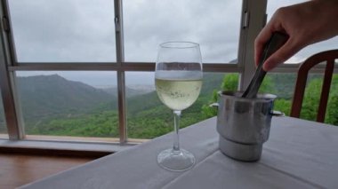 Restoranın masasındaki beyaz şaraba buz koyan bir adamın eli. Arka planda dağlar olan güzel bir manzara. Yavaş çekim videosu. 