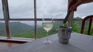 Restoranın masasındaki beyaz şaraba buz koyan bir adamın eli. Arka planda dağlar olan güzel bir manzara. Yavaş çekim videosu. 