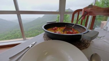 Geleneksel İspanyol yemeği. Istakozlu Paella. Valencia 'dan lezzetli yemekler. Arka planda dağlar olan güzel bir manzara. Elin tabağa yemek koyuyor. Yavaş çekim videosu. 