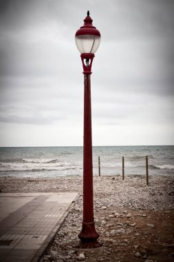Bulutlu bir günde deniz kenarında kırmızı bir lamba direği.