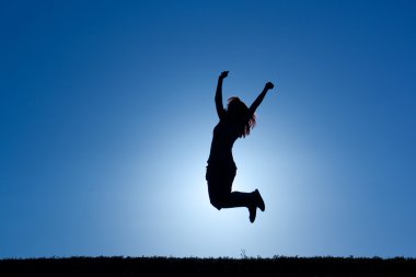 Güneşin altındaki bir kadının silueti zaferle zıplıyor