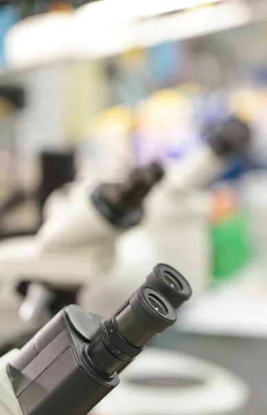 Microscope eyepieces in a lab, with out of focus lab equipment backdrop — Stock Photo, Image