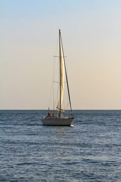 Un velero que viaja hacia el atardecer, cálido resplandor proveniente del horizonte — Foto de Stock