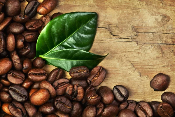 Granos de café y hojas en el fondo de madera —  Fotos de Stock