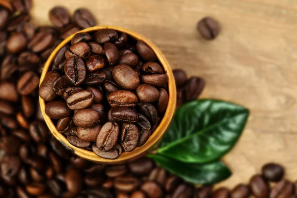 Grãos de café e folhas no fundo de madeira — Fotografia de Stock