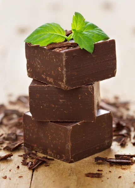 Gros morceaux de pièces de chocolat et feuilles de menthe sur bac en bois Images De Stock Libres De Droits