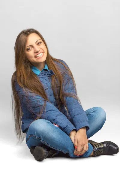 Mujer casual joven en una chaqueta sentada en el suelo. Sonriendo. . — Foto de Stock