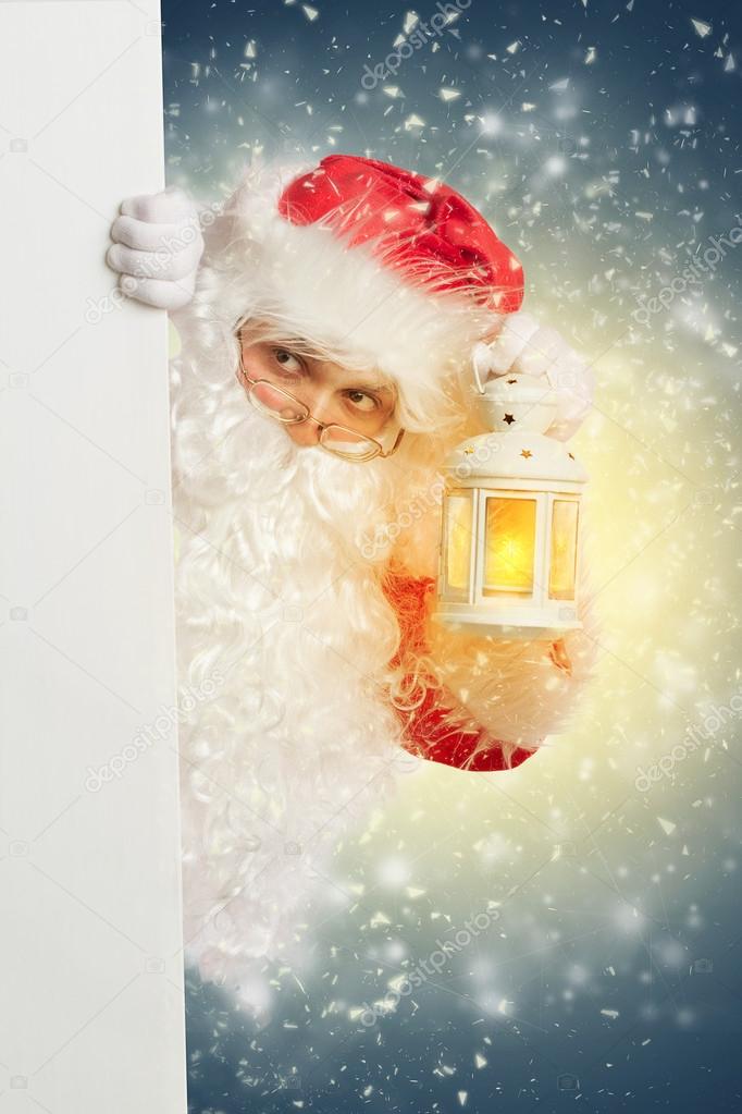 Santa Claus looking from behind white blank banner holding a shi