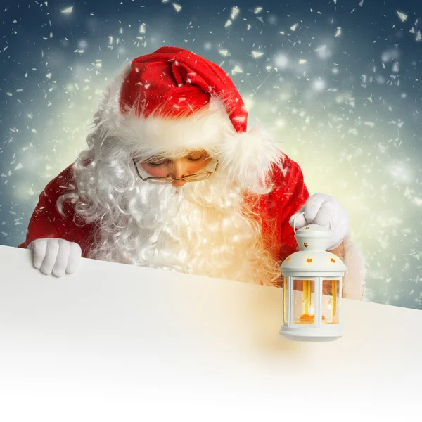 Santa Claus mirando hacia abajo en la pancarta blanca en blanco sosteniendo un brillo —  Fotos de Stock