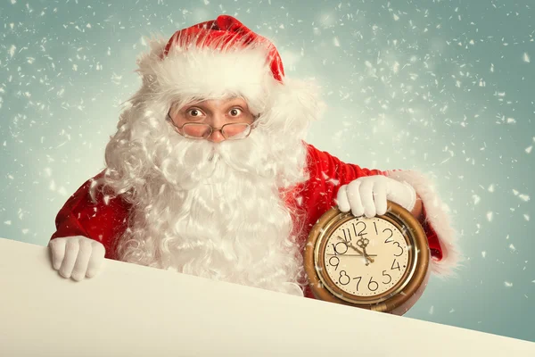 Santa Claus with white blank banner holding a clock showing sev — Stock Photo, Image