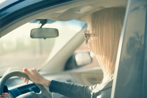 Ξανθιά γυναίκα με ένα γυαλιά ηλίου για την οδήγηση ενός αυτοκινήτου. Δύση του ηλίου φως, t — Φωτογραφία Αρχείου