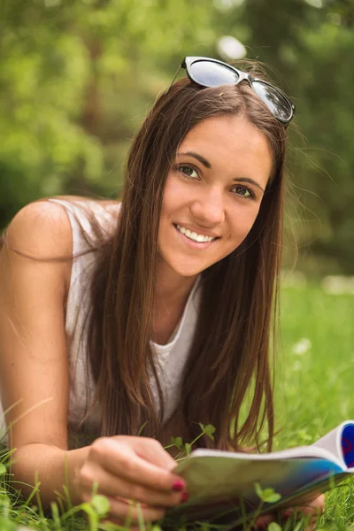 Eine junge brünette Frau liegt mit einem Magazin im Gras — Stockfoto