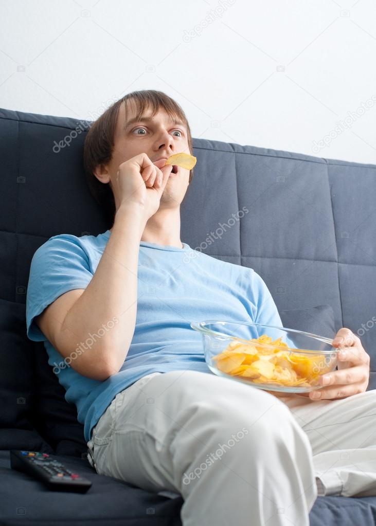 Young man watching tv and eating chips