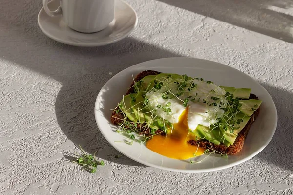 Healthy breakfast, toasted whole grain bread with avocado, poached egg, microgreens and a cup of coffee