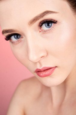 Kırmızı arka planda kirpikleri için makyaj yapan güzel bir genç kadın. Sağlıklı deri portresi