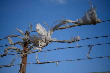 Dikenli tel örgü ve yanında enkaz parçaları. Koruyucu bir çitin dikenli tellerinin dikenli iğnelerinde parçalanmış plastik torbalar.