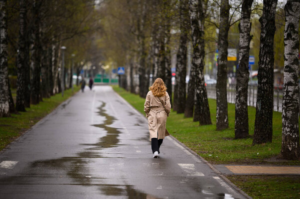 Young woman walks down the street in spring. Girl in a coat walks. Back view.