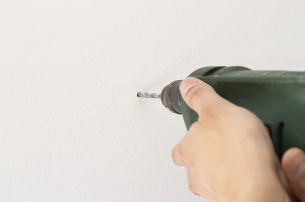 Closeup of a man drilling a hole in wall white and space copy — Stock Photo, Image