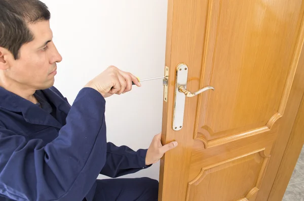 Carpinteiro fixando uma fechadura na porta com uma chave de fenda — Fotografia de Stock