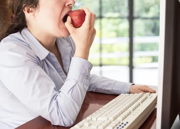 Kvinnan arbetar på en dator och äta ett äpple röd — Stockfoto