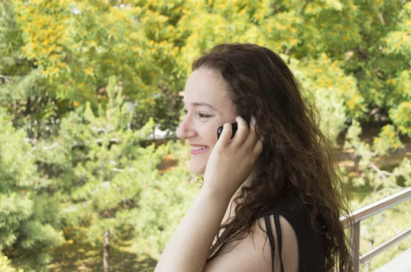 Žena mluví do mobilu zároveň s výhledem do zahrady — Stock fotografie