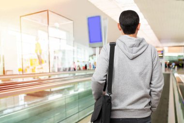 Rearview shot of an unrecognizable young man standing on a moving walkway in the airport