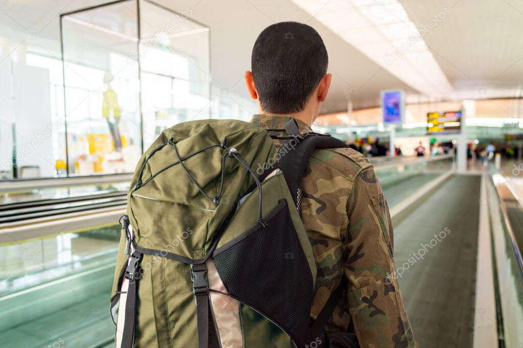Rearview shot of an unrecognizablesoldier in a military uniform standing on a moving walkway in the airport