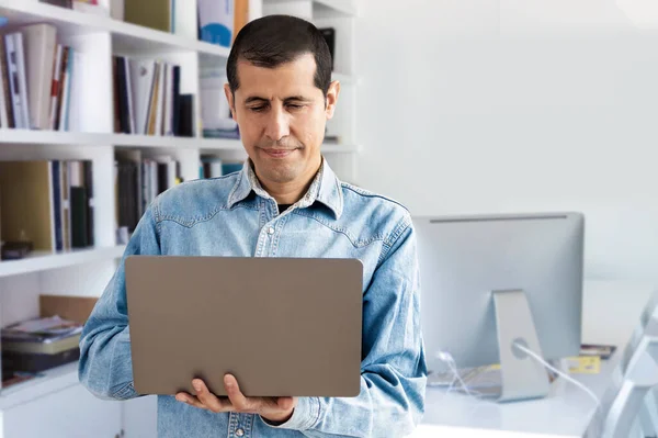 一个年轻英俊商人站在办公室时在笔记本电脑上工作的剪影 — 图库照片