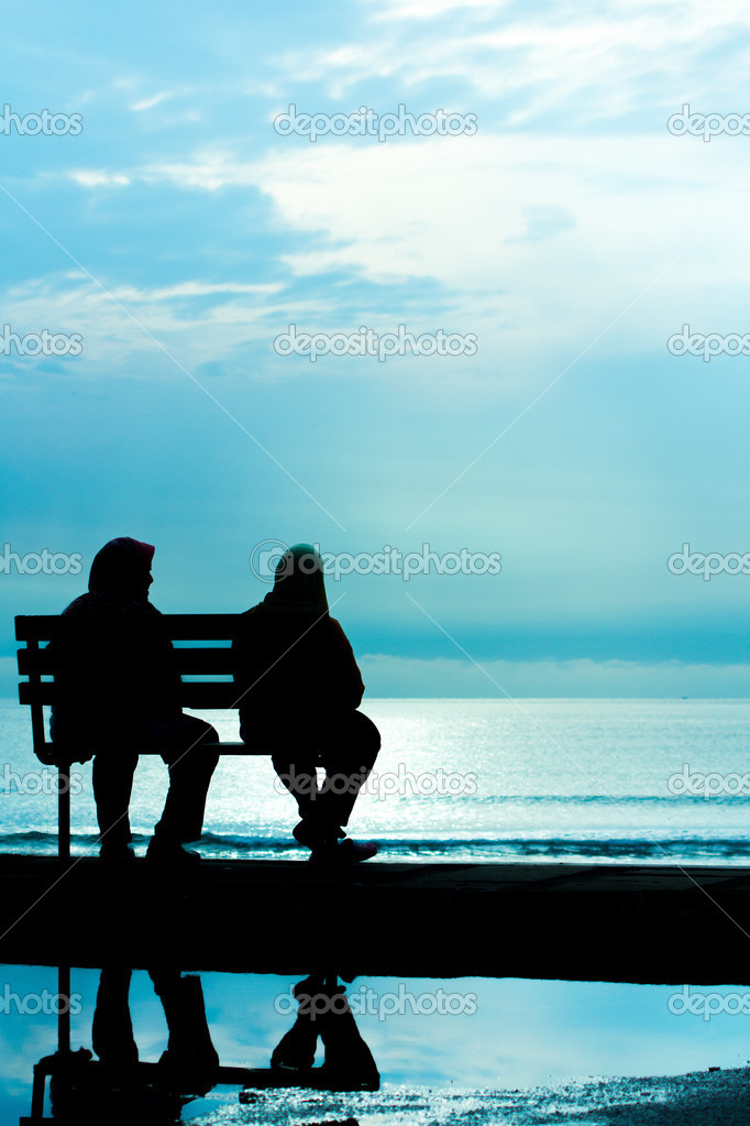 Two friends sitting on wood bench near beach