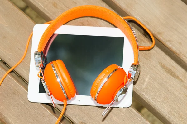 White tablet PC with orange headphones on the wood bench — Stock Photo, Image