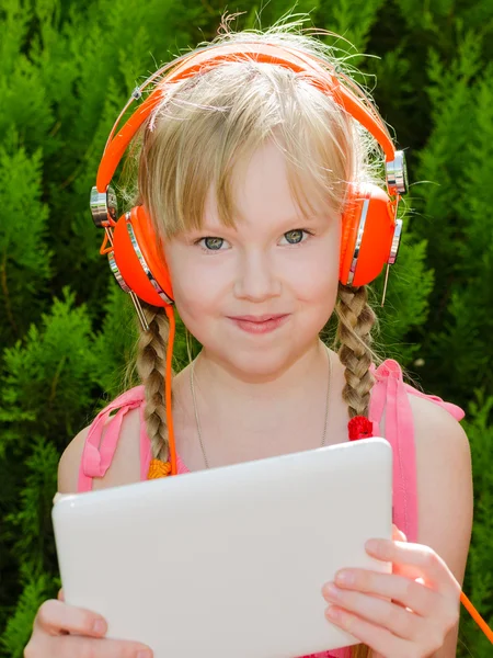 Linda chica con tablet pc escuchar música en los auriculares — Foto de Stock