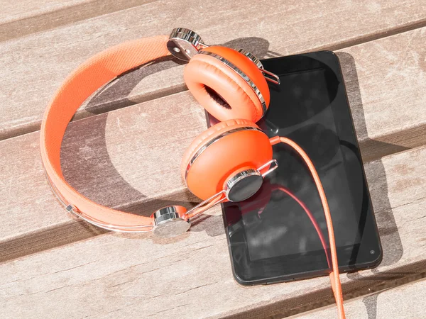 Vibrant orange headphones and black tablet pc on wooden bench — Stock Photo, Image