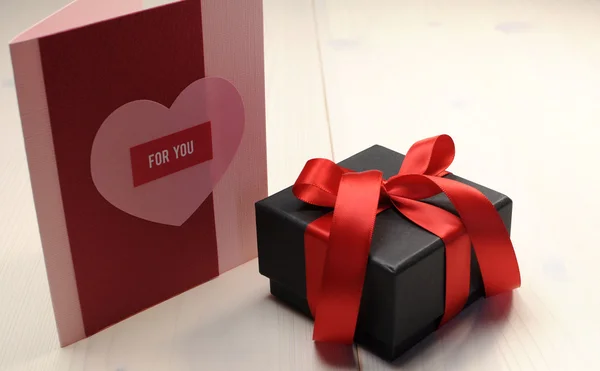 Handgemachte Geschenkkarte, "für Sie", mit schwarzem Schachtel-Geschenk und roter Schleife auf weißem Naturholztisch. — Stockfoto