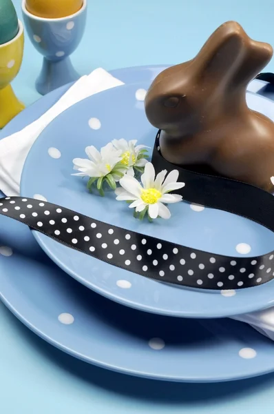 Feliz cena de Pascua con platos de lunares azules y decoraciones sobre un fondo azul. Primer plano vertical con conejo de Pascua de chocolate . —  Fotos de Stock